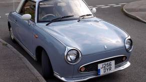 A Nissan Figaro parked on the side of the street.