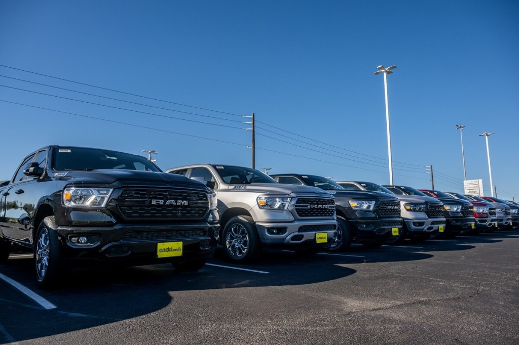 A lot of used RAM 1500 trucks and other used cars sit under the sun.