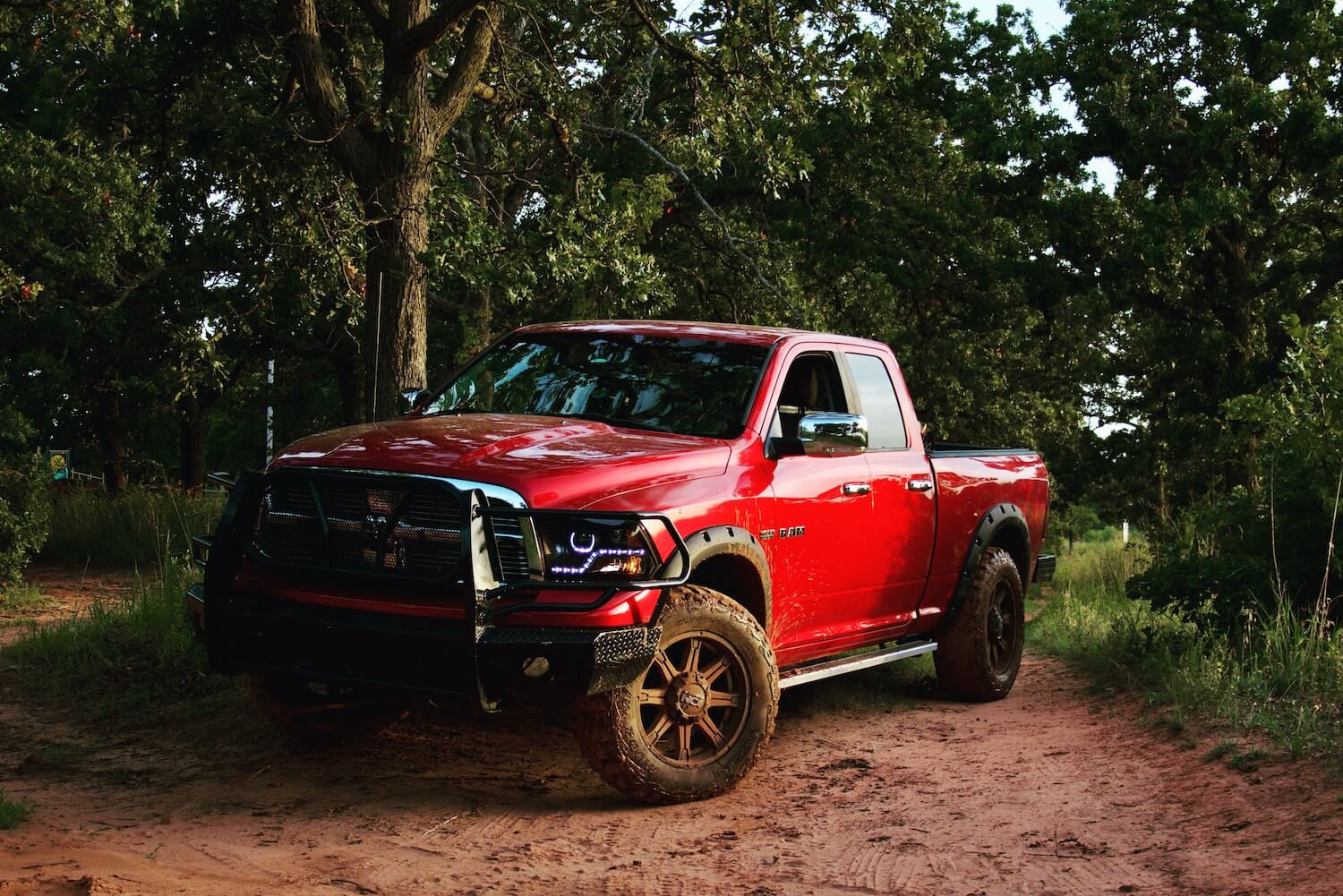 Red 4th-gen Ram 1500 pickup truck parked on a dirt trail in the woods.