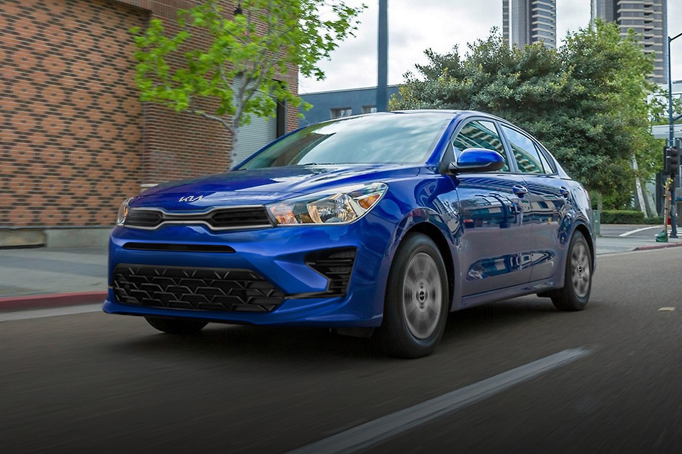 A blue 2023 Kia Rio driving on a city street. The Rio is one of two new cars under $20,000