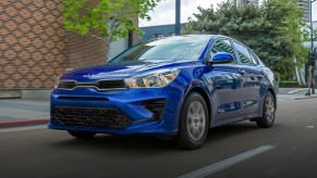 A blue 2023 Kia Rio driving on a city street. The Rio is one of two new cars under $20,000