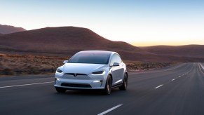 A white Tesla Model X midsize electric SUV is driving on the road.