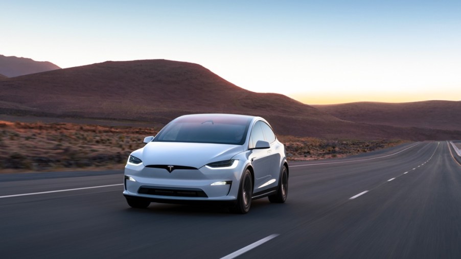 A white Tesla Model X midsize electric SUV is driving on the road.