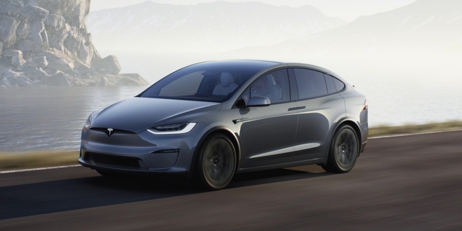 A gray Tesla Model X midsize SUV is driving on the road. 