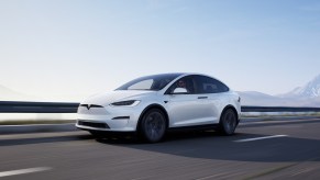 A white Tesla Model X driving along a road. Tesla sales data for the Model X reveal it's not the least popular model.