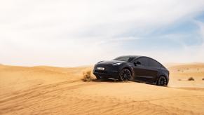 A black Tesla Model Y driving on desert sand. Tesla Model Y sales figures show it to be the best-selling vehicle in America