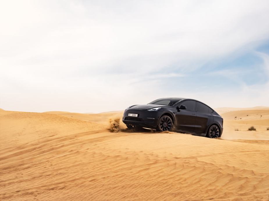 A black Tesla Model Y driving on desert sand. Tesla Model Y sales figures show it to be the best-selling vehicle in America