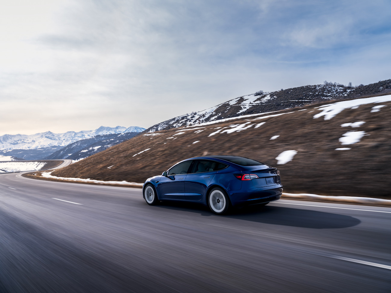 A blue Tesla Model 3 driving along a snowy mountain road. Tesla price cuts have affected the Model 3 also