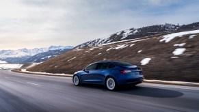 A blue Tesla Model 3 driving along a snowy mountain road. Tesla price cuts have affected the Model 3 also