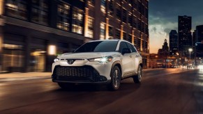 A white 2023 Toyota Corolla Cross subcompact SUV is driving down the road at night.