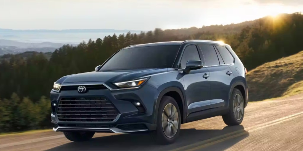 A blue 2024 Toyota Grand Highlander three-row midsize SUV is driving on the row.