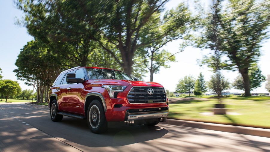 A red 2023 Toyota Sequoia driving down a shaded road on a sunny day. This Toyota SUV is gaining in popularity