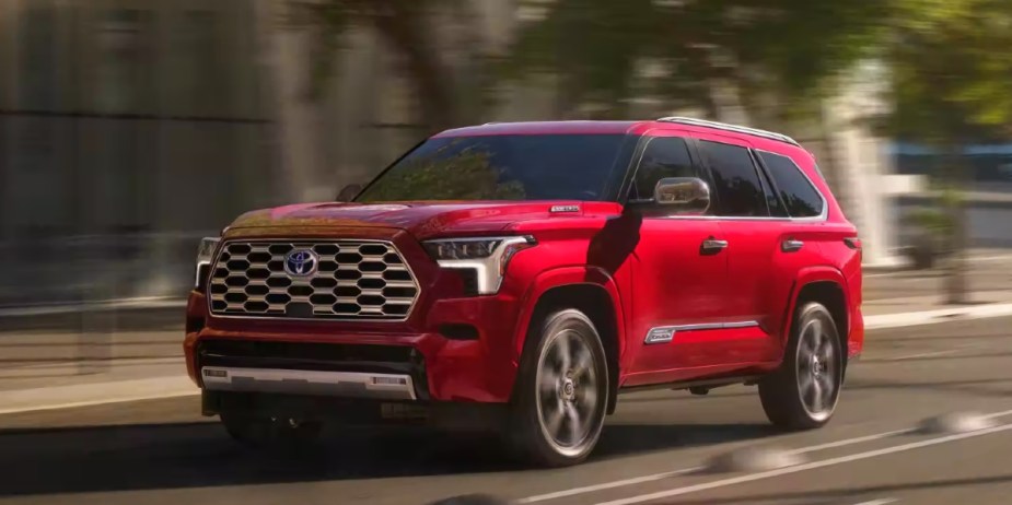A red 2024 Toyota Sequoia full-size SUV is driving on the road. 