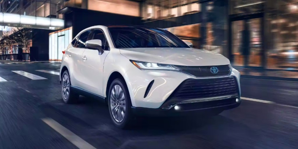 A white 2023 Toyota Venza midsize hybrid SUV is driving on the road.