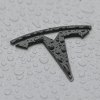 The black logo on a silver used Tesla electric car parked in the rain.