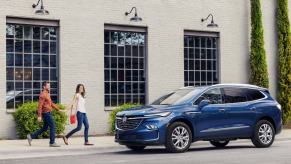 A 2024 Buick Enclave midsize SUV in Emperor Blue Metallic in front of a white brick building as a couple approaches