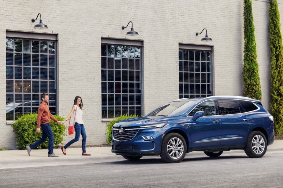 A 2024 Buick Enclave midsize SUV in Emperor Blue Metallic in front of a white brick building as a couple approaches