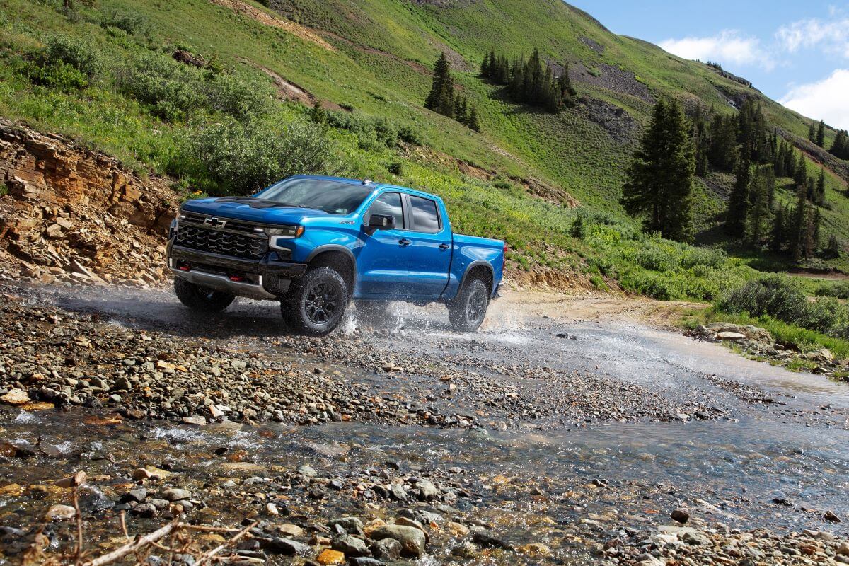 A 2024 Chevy Silverado ZR2 full-size pickup truck model driving on wet and river-run gravel and rocks