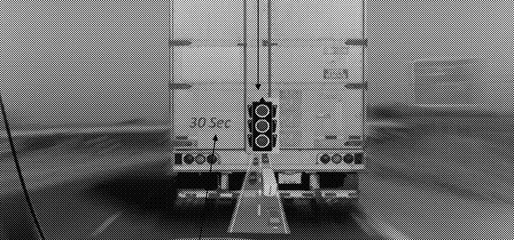 A black and white photo of a traffic light seen "through" a semi truck tailgate. 
