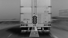 A black and white photo of a traffic light seen "through" a semi truck tailgate.