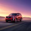 The 2024 Cadillac XT6 Sport midsize luxury SUV model driving on a highway at sunset