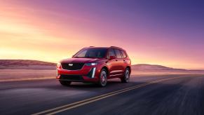 The 2024 Cadillac XT6 Sport midsize luxury SUV model driving on a highway at sunset