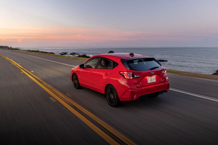 A rear side shot of a 2024 Subaru Impreza RS hatchback model driving on a highway past the sea