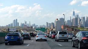 A row of cars waiting in stop-and-go traffic, the Manhattan skyline visible behind.