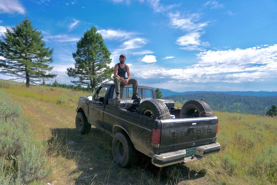 Automotive journalist Henry Cesari sitting on his 1988 Ford F-150 parked in a field during an overlanding camping expedition.
