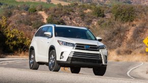 A white 2018 Toyota Highlander Hybrid midsize SUV is driving on the road.