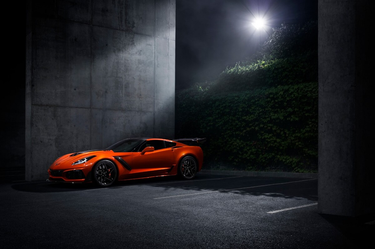 A bright-orange Corvette parks in a garage under the moon.