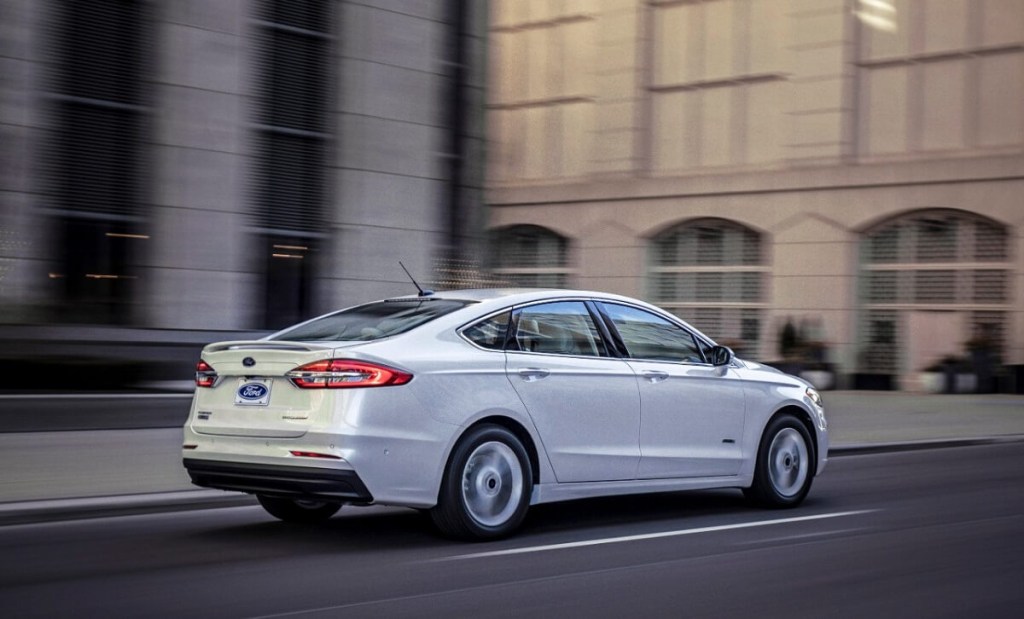 A white 2020 Ford Fusion drives by city structures.