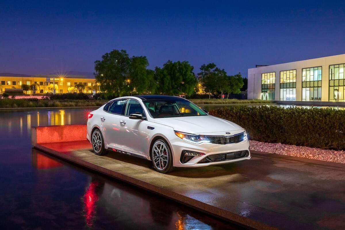 A white 2020 Kia Optima parked outside a modern two-story building next to a lake at night