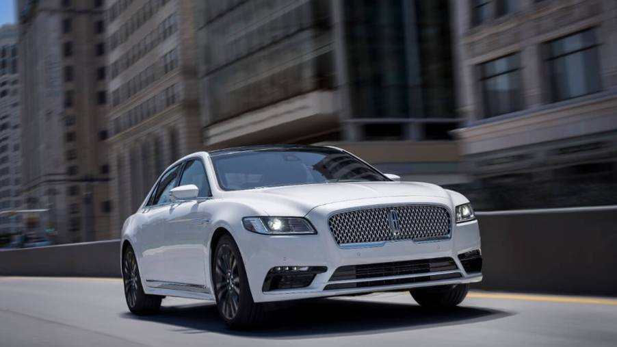 A used white Lincoln Continental luxury car cruises down city streets.
