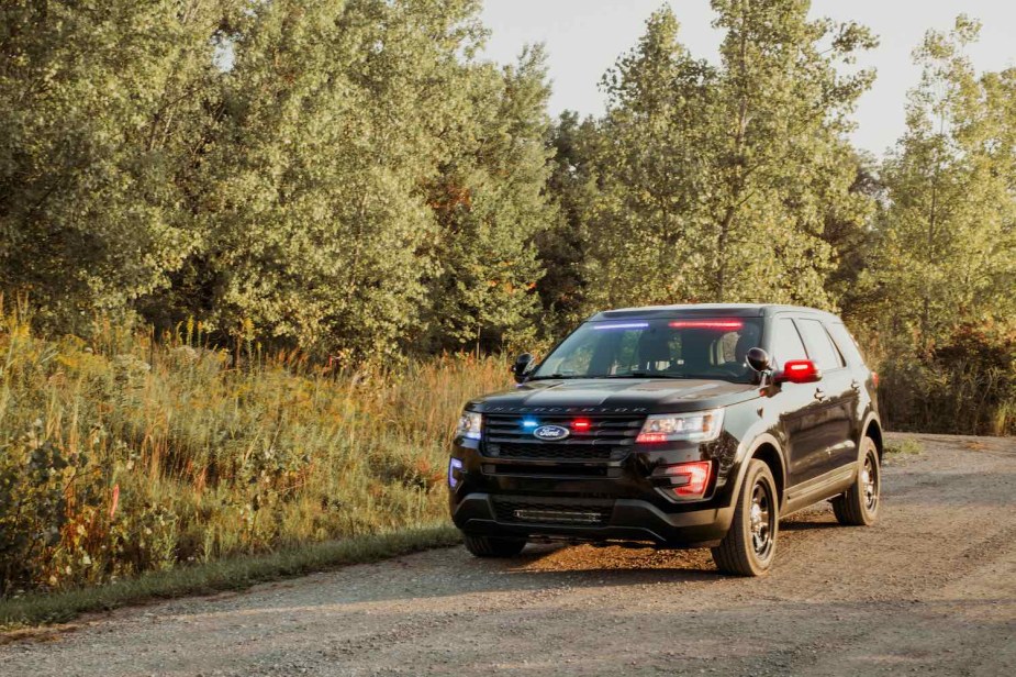 A black Ford police cruiser parked on a rural road, trees visible in the background.