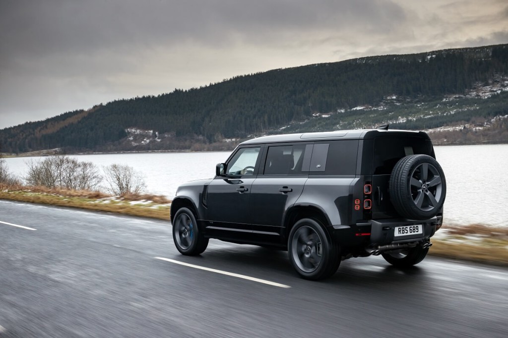 A dark-gray 2022 Land Rover Defender 110 V8 shows off its rear-end styling while it drives by the lake.