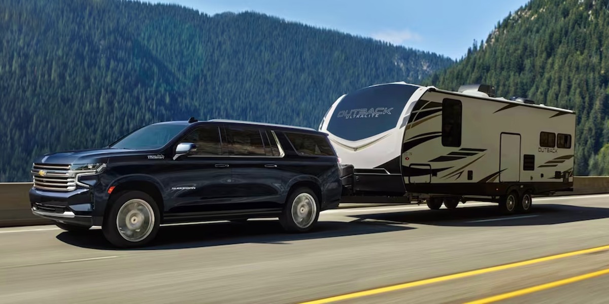 A black 2023 Chevrolet Suburban full-size SUV is towing a trailer.