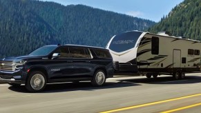 A black 2023 Chevrolet Suburban full-size SUV is towing a trailer.
