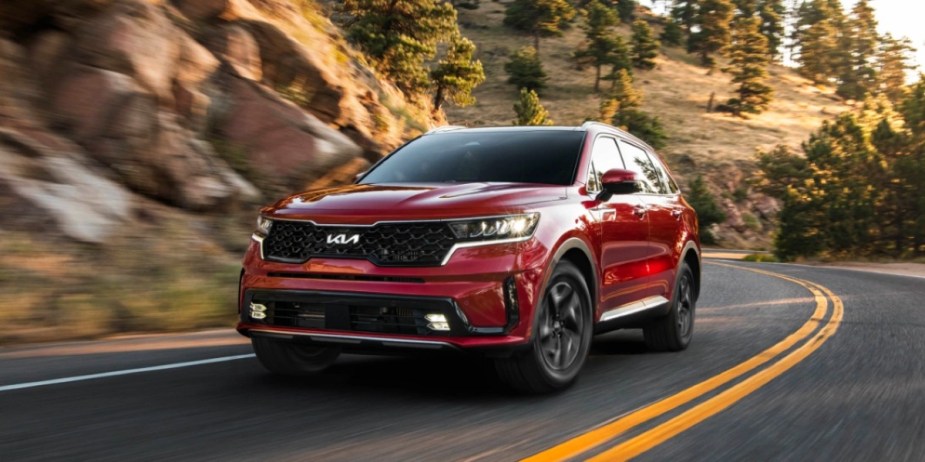 A red 2023 Kia Sorento Hybrid midsize hybrid SUV is driving on the road. 