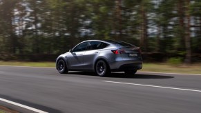 A gray 2023 Tesla Model Y small electric SUV is driving on the road.