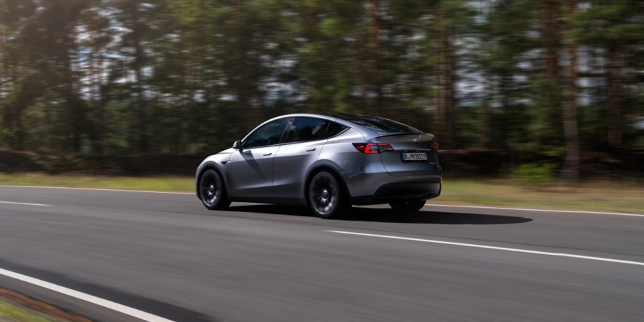 A gray 2023 Tesla Model Y small electric SUV is driving on the road.