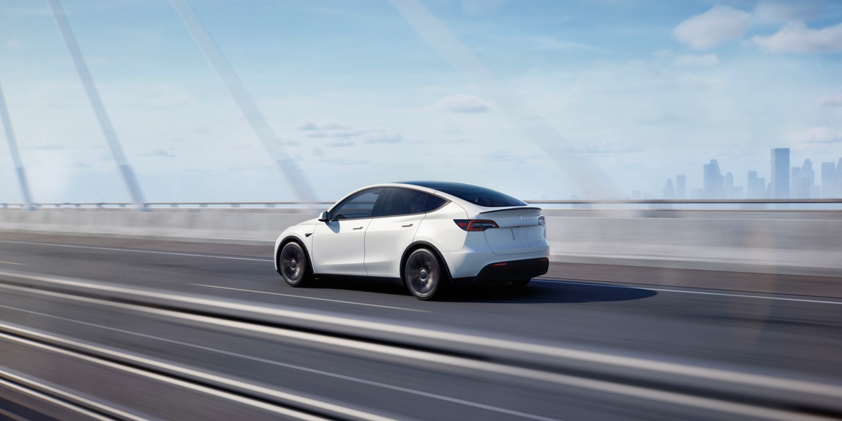 A white 2023 Tesla Model Y small electric SUV is driving on the road.