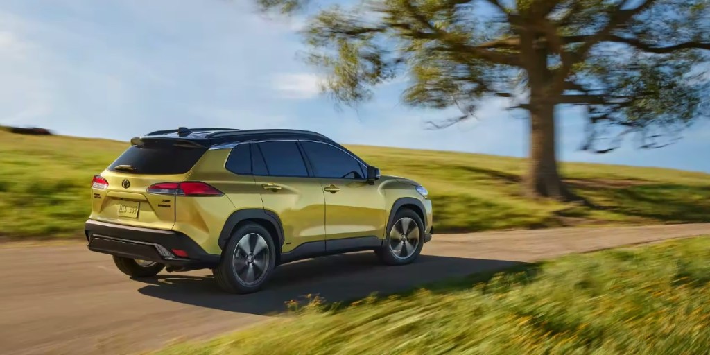 A gold 2023 Toyota Corolla Cross Hybrid subcompact hybrid SUV is driving on the road.