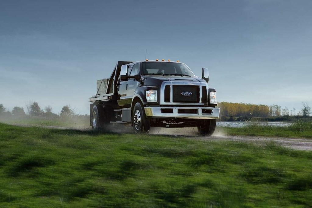 A 2024 Ford F-650 commercial truck drives on a dirt road while carrying payload on its flatbed