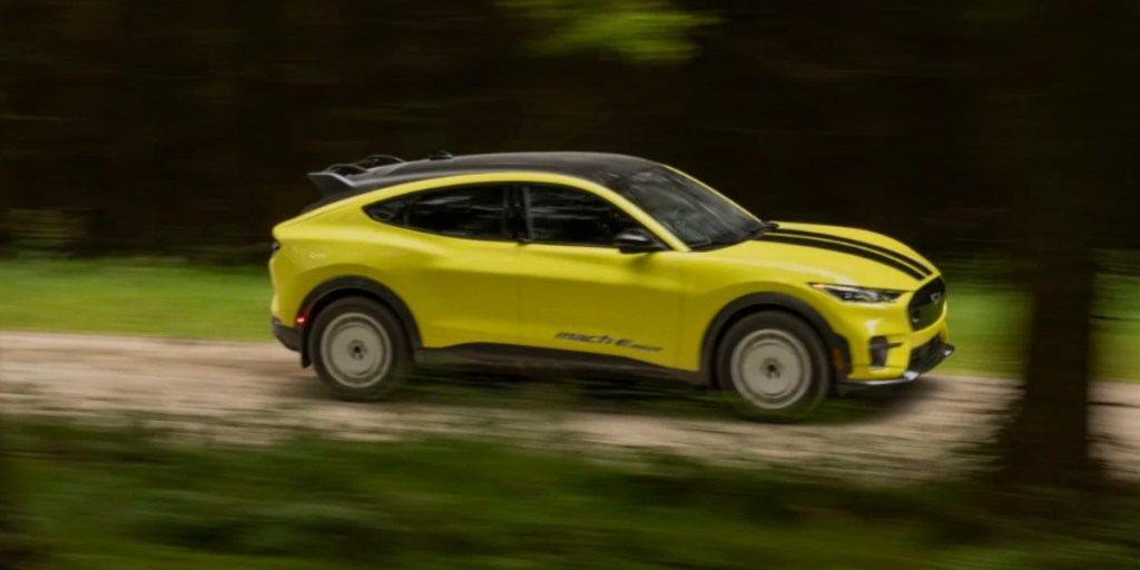 A yellow 2024 Ford Mustang Mach-E Rally small electric SUV is driving off-road.