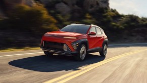 An orange 2024 Hyundai Kona subcompact SUV is driving on the road.