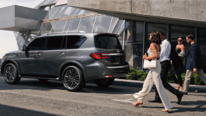 A side profile shot of a parked 2024 Infiniti QX80 full-size luxury SUV model as people walk toward it