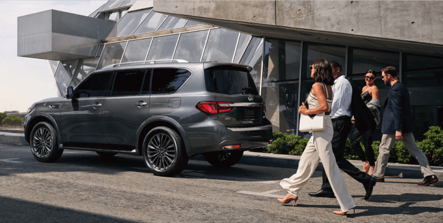 A side profile shot of a parked 2024 Infiniti QX80 full-size luxury SUV model as people walk toward it