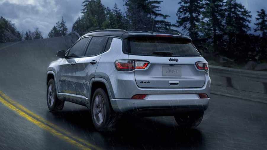 The rear of a silver 2024 Jeep Compass Trailhawk driving on a rainy road.