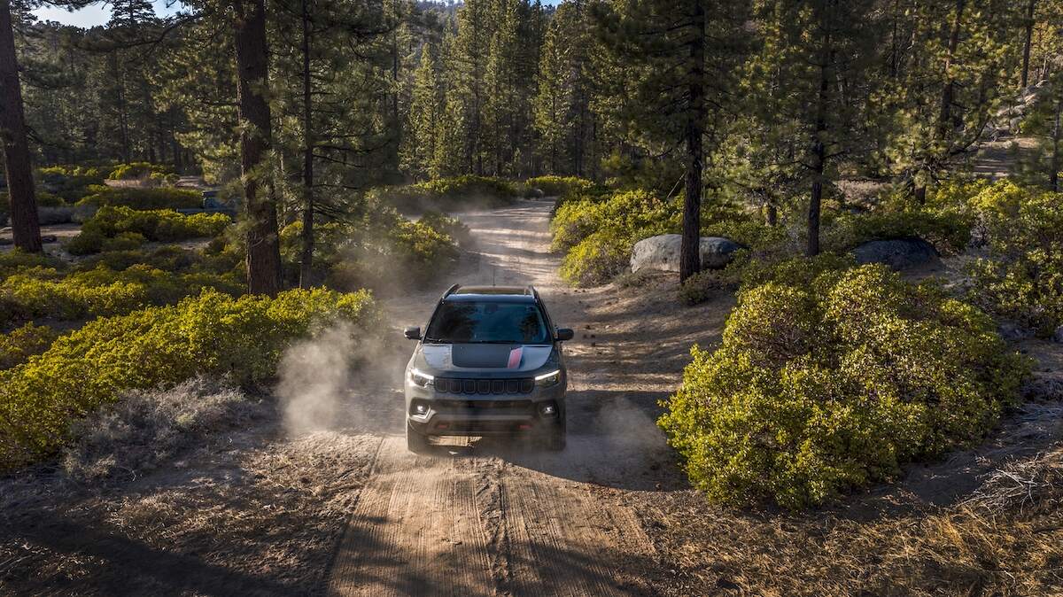 A gray and black 2024 Jeep Compass Trailhawk drives on a dirt road in the woods